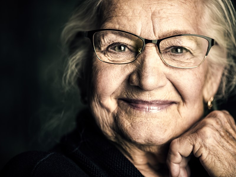 An older woman with glasses smiling and looking at camera
